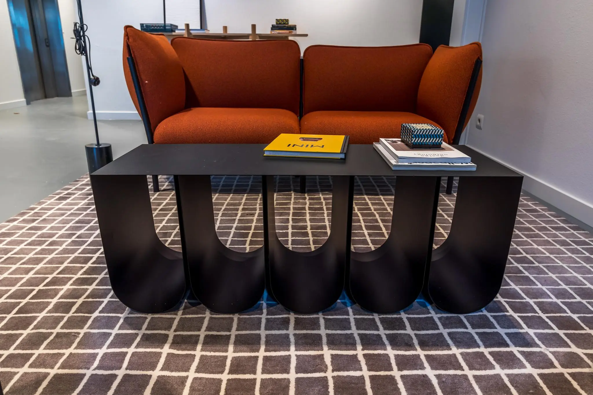 Moderne zithoek met een oranje bank, zwart designer salontafel en boeken op een geruit vloerkleed.